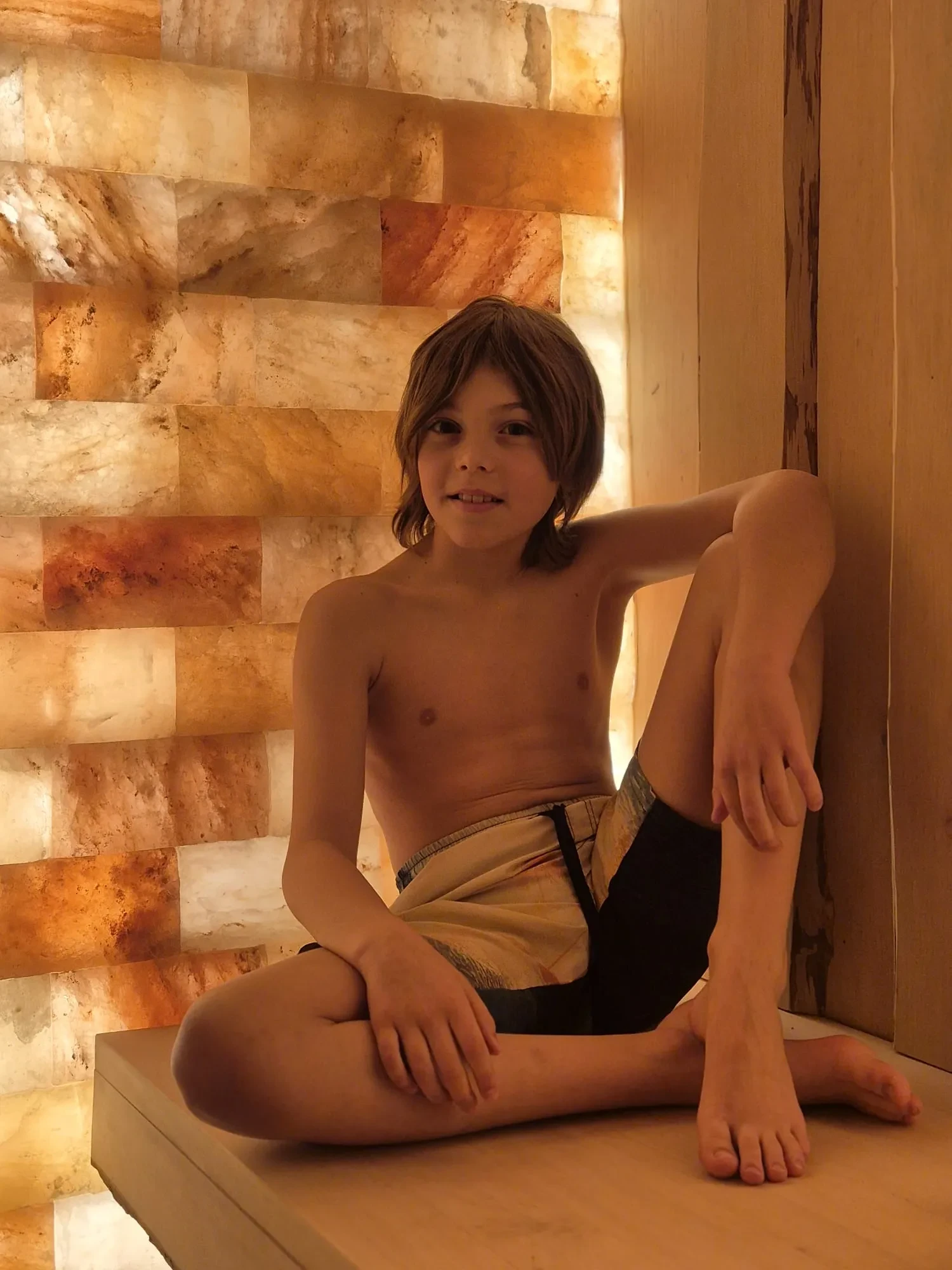 Enfant assis dans sauna avec mur éclairé.
