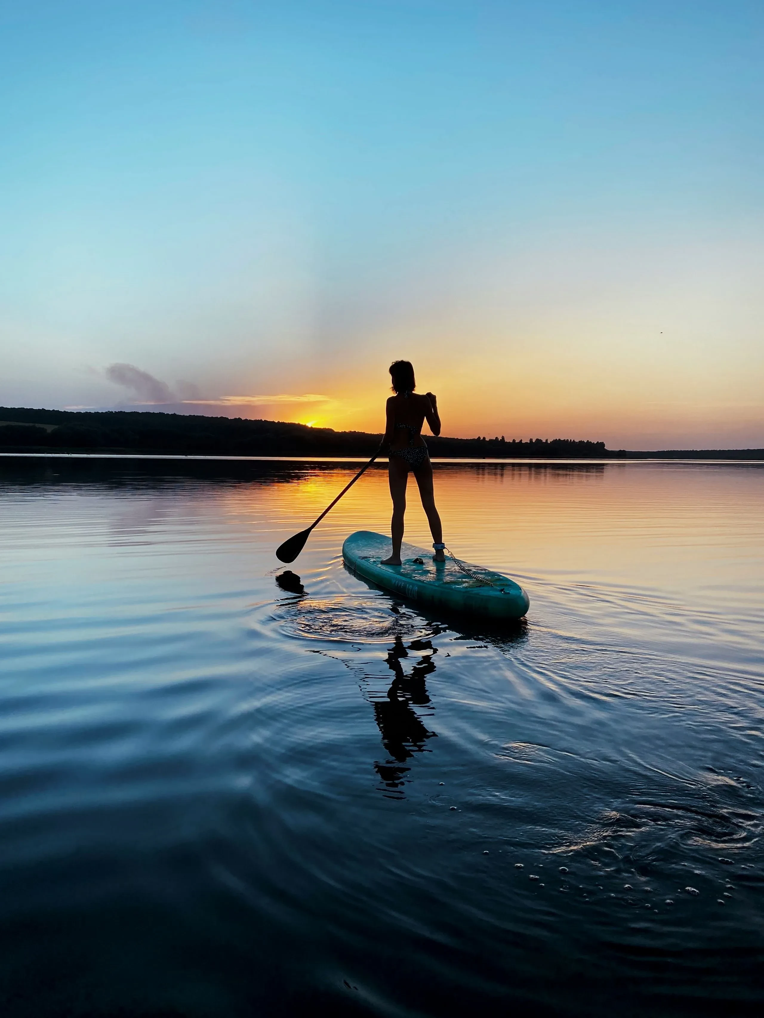 Personne sur paddle au coucher de soleil sur lac.