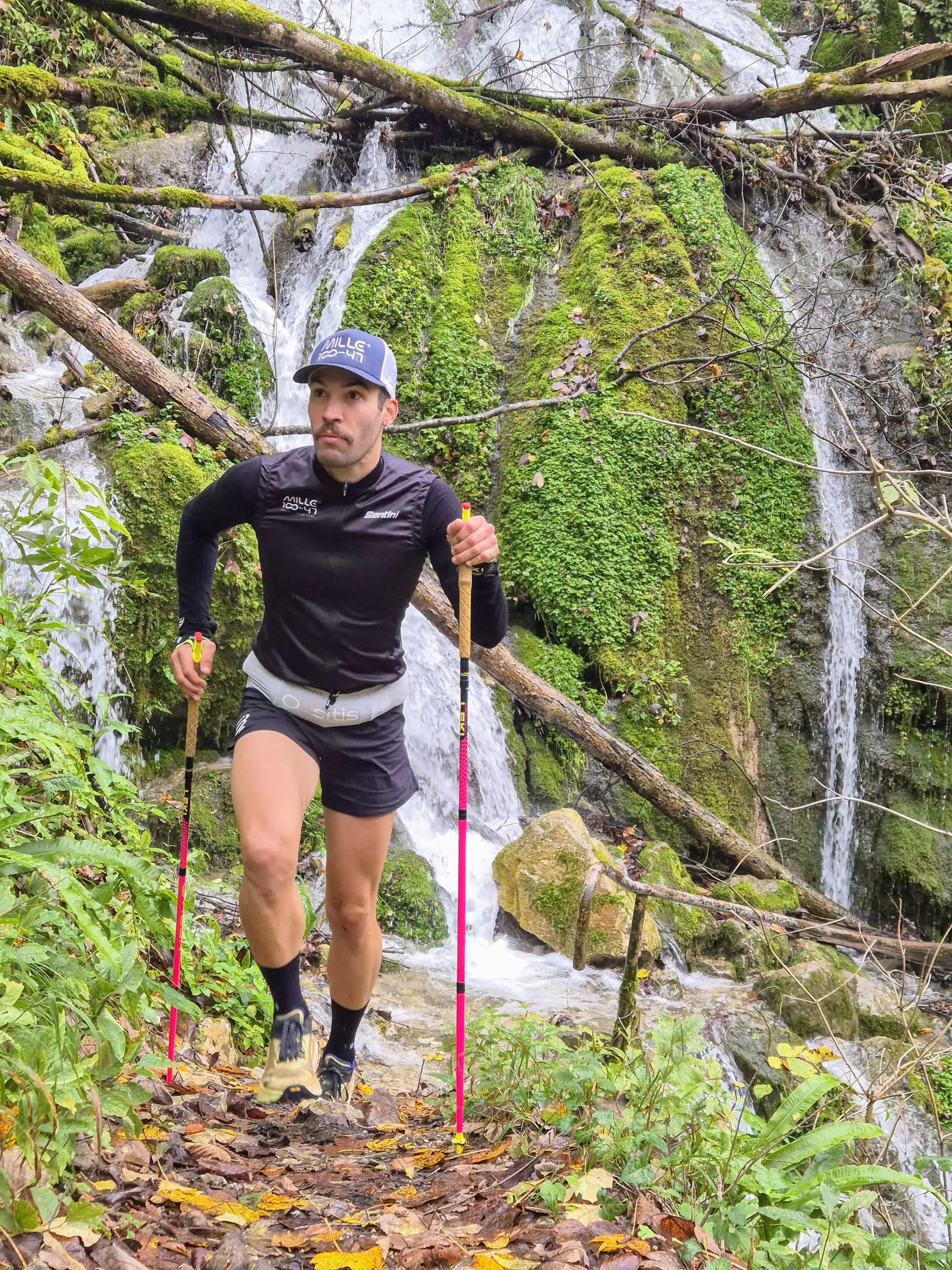 Homme courant avec bâtons devant une cascade.